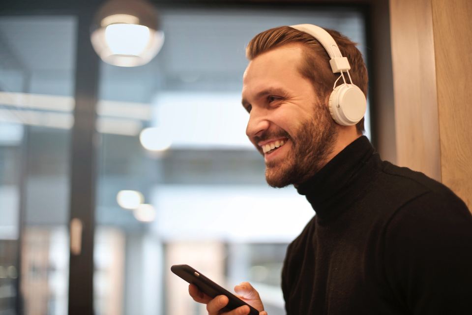 Smiling man wearing white over-ear headphones while checking his phone