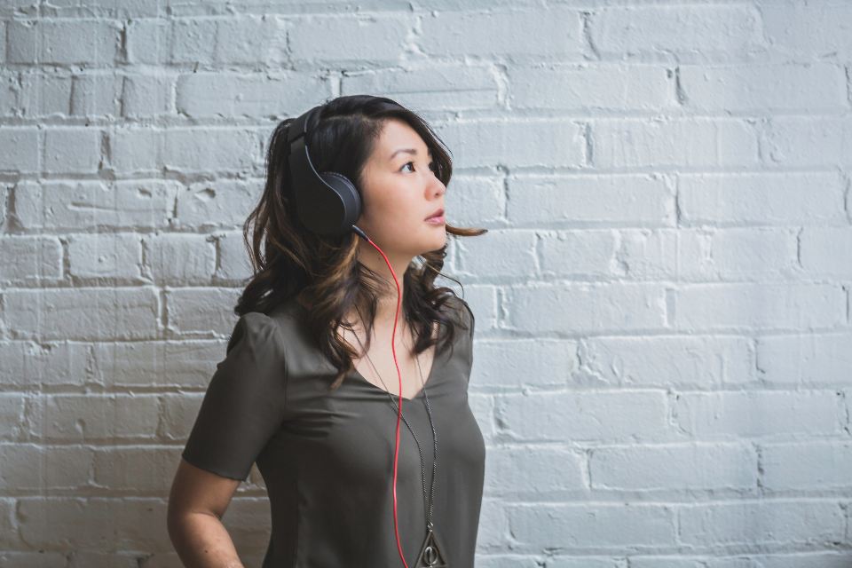 Woman wearing headphones leaning against a white brick wall