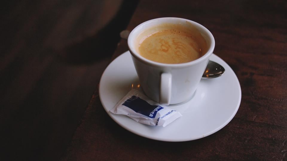An espresso in a white cup and saucer on a dark table