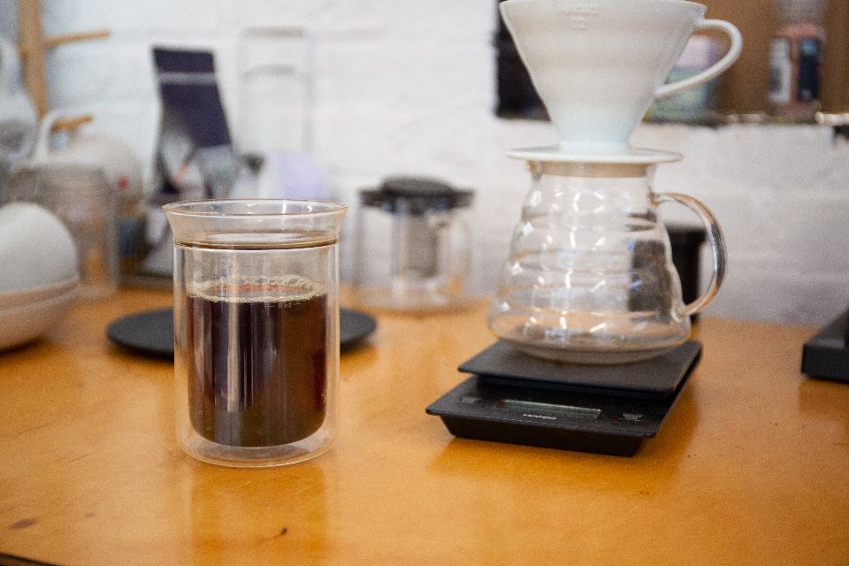 Pour-over coffee in a glass beside a dripper and scale