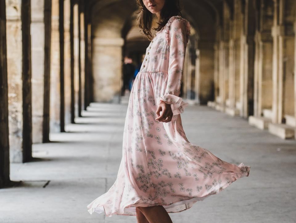 Woman in a long blush floral dress twirling through a stone arcade