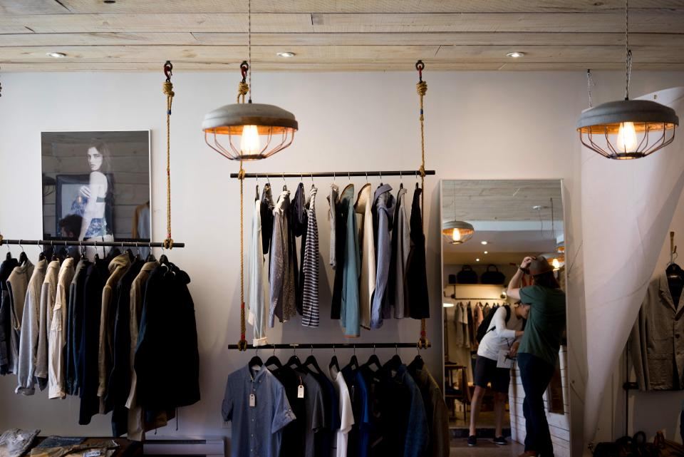 A boutique rail of hanging garments under pendant lamps