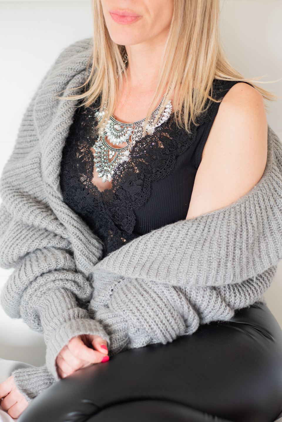 Woman in a grey chunky-knit cardigan over a black lace top