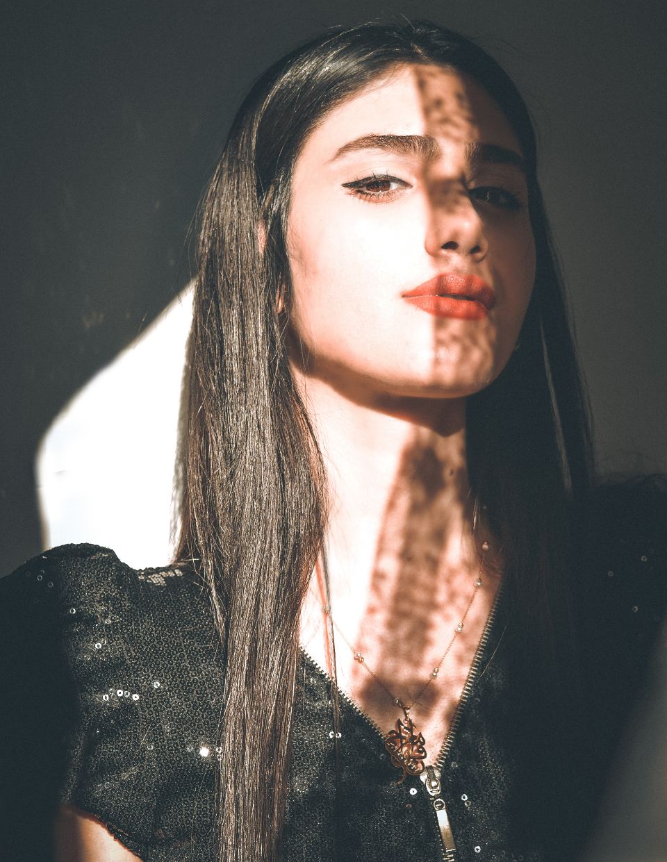 Portrait of a woman with long dark hair, leaf shadows across her face