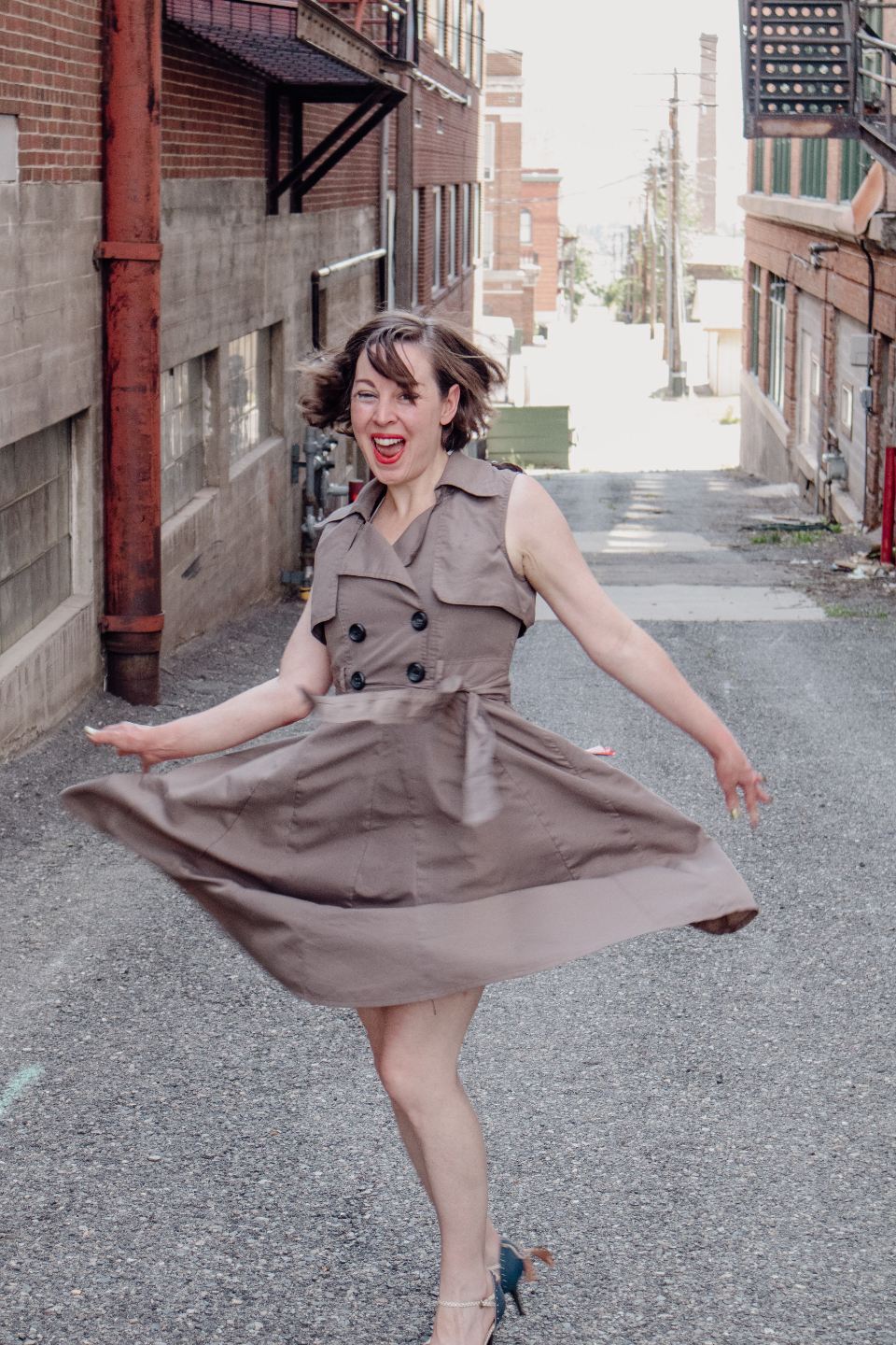 Woman twirling in a taupe belted shirt dress in a narrow alley