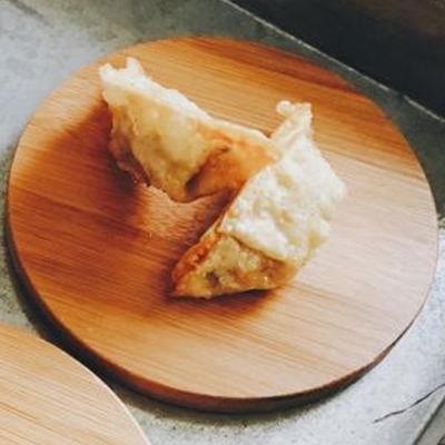 Two golden fried dumplings on a round bamboo coaster