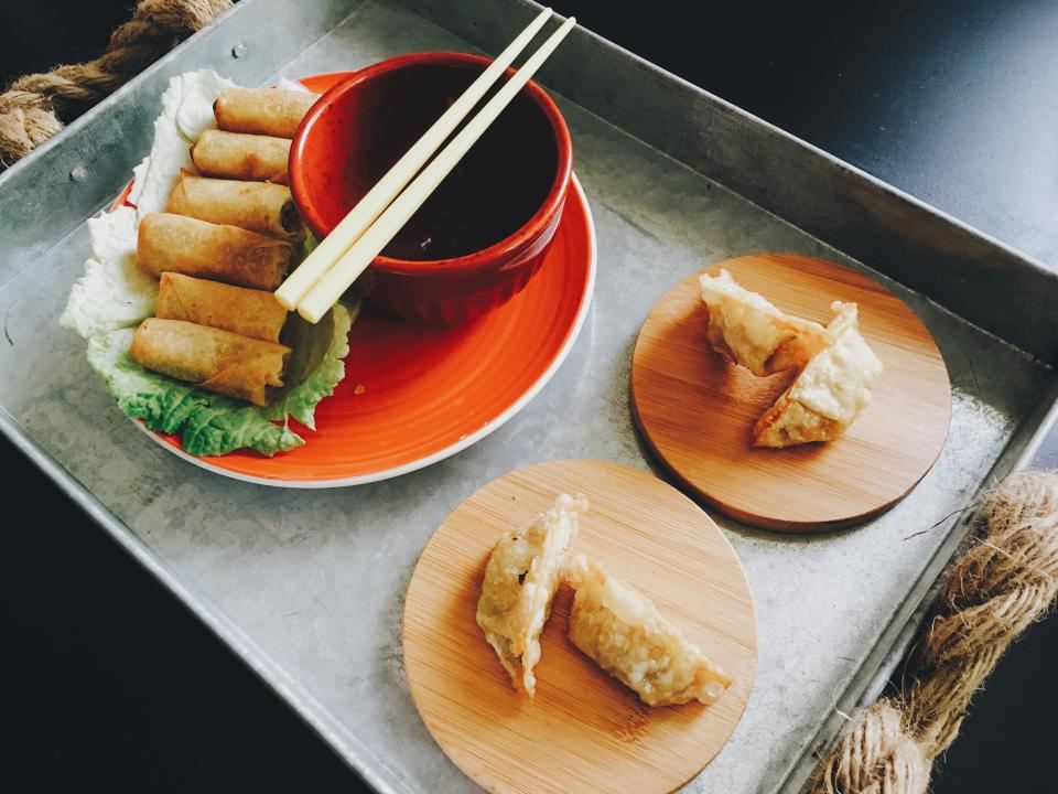 Fried dumplings on round bamboo coasters beside spring rolls and a dipping sauce