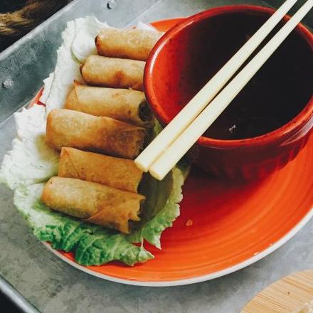 Spring rolls on lettuce with a red bowl of dipping sauce and chopsticks