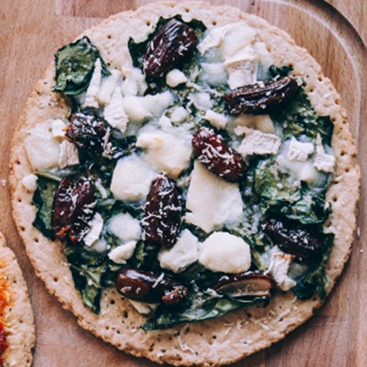 White-base pizza with spinach, soft white cheese and dark roasted dates, from above