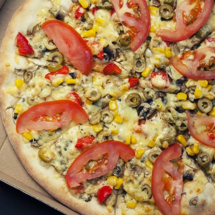 Close-up of a pizza topped with tomato slices, sweet corn, green olives, mushrooms and red pepper
