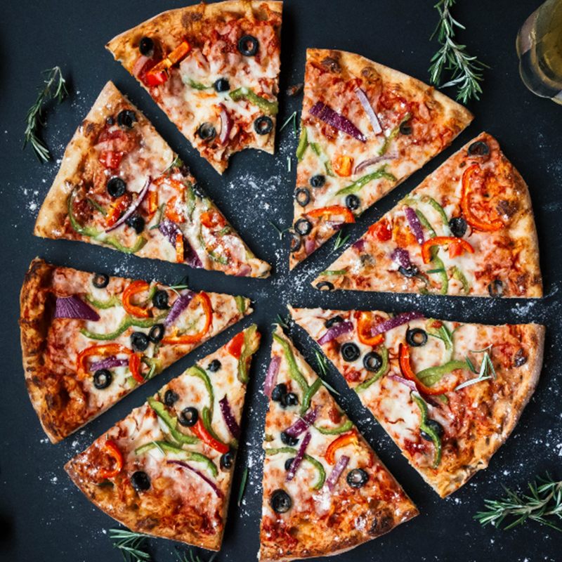 Top-down view of a sliced pizza with peppers, red onion, black olives and mozzarella