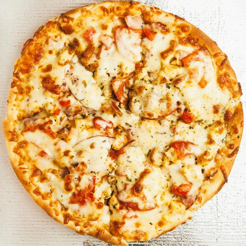 Whole pizza with chicken, ham slices, tomato and oregano under golden, browned mozzarella