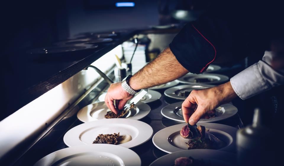 A chef placing garnish on a row of plates at the pass