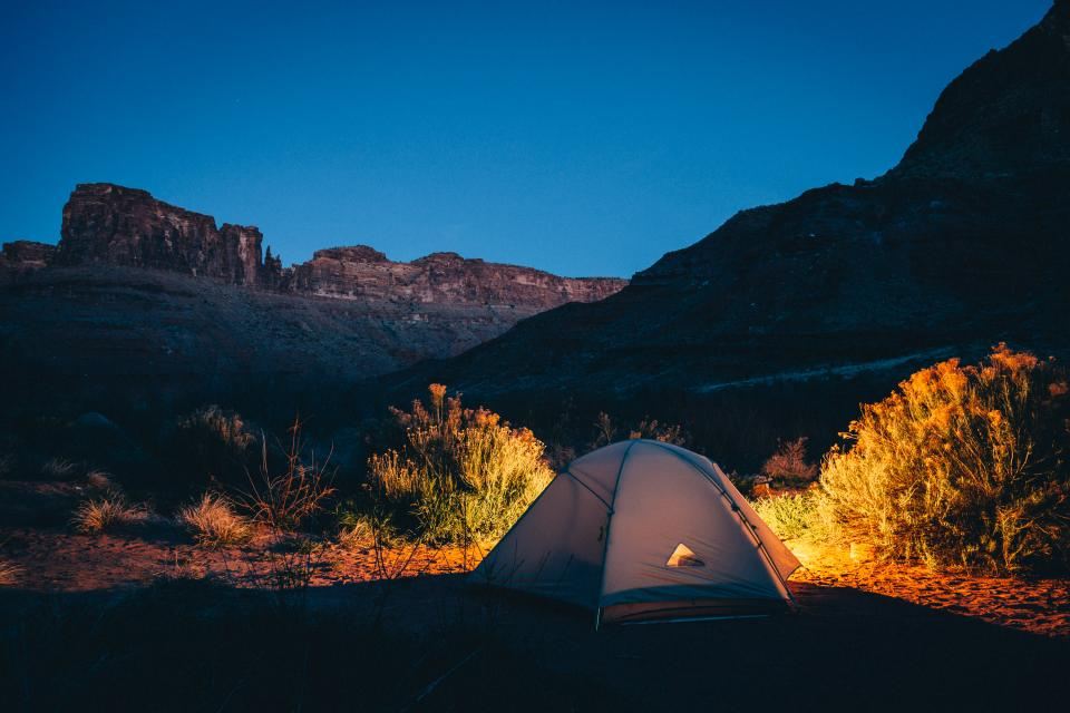 An orange tent glowing at dusk below a mountain ridge