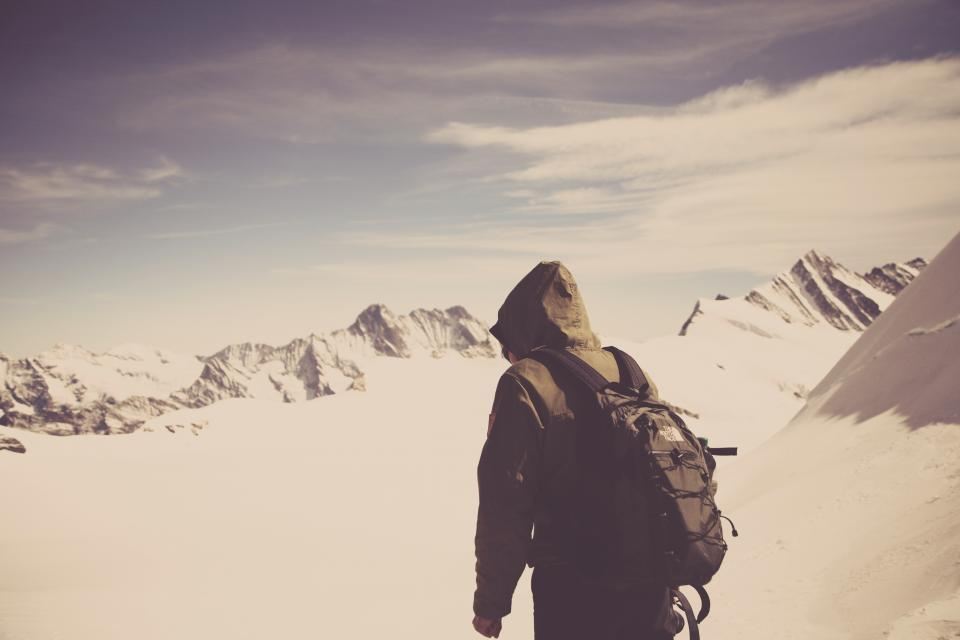 A trekker with a backpack looking out over snow-covered peaks