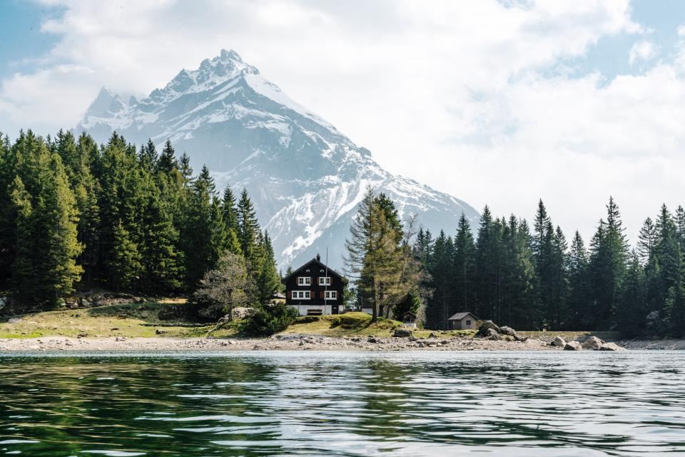 Snow-covered pine forest and a wooden hut beside a frozen lake