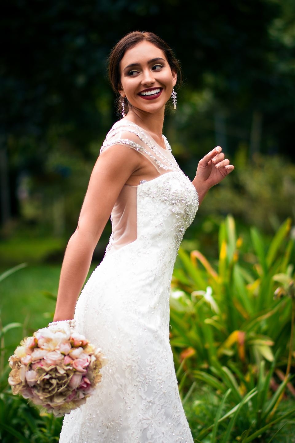 Smiling bride in a lace gown holding a bouquet in a garden