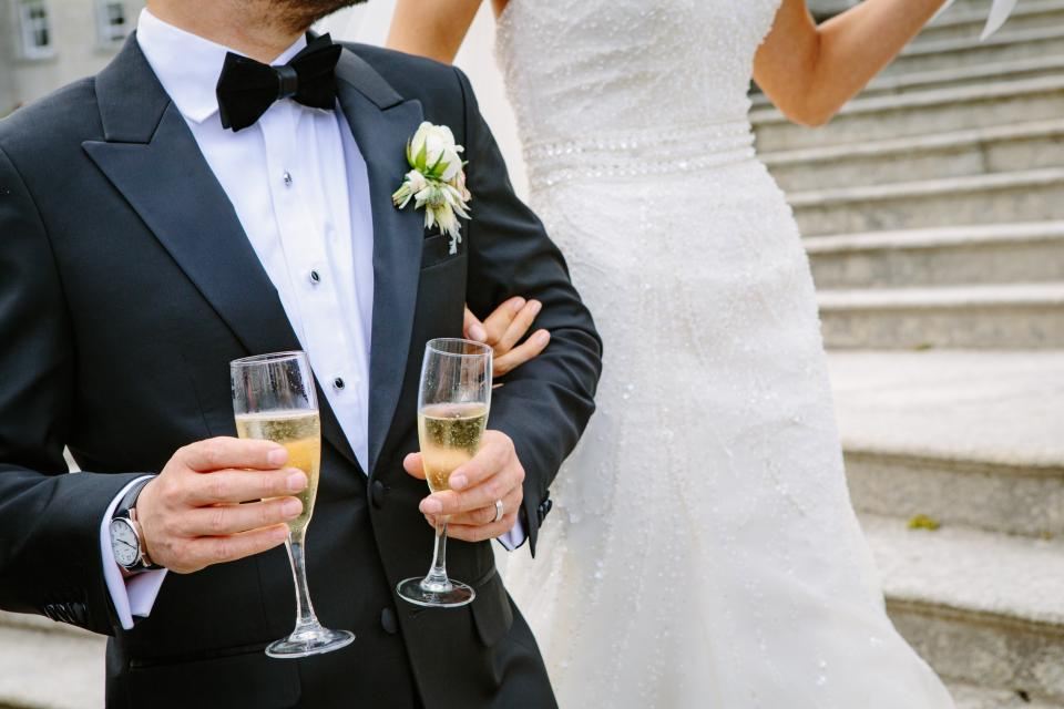 Groom holding two glasses of champagne beside the bride on steps