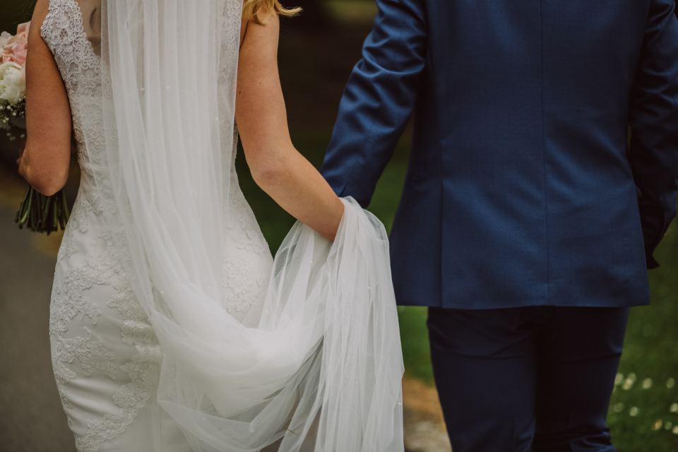 Bride and groom walking away together, veil trailing