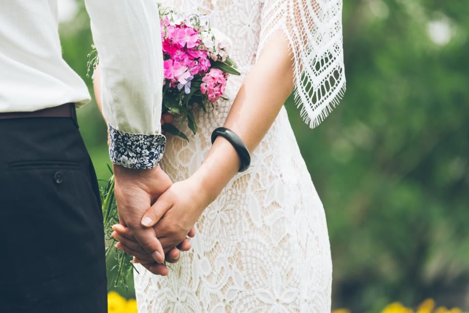 Bride and groom holding hands, her lace sleeve beside his cuff